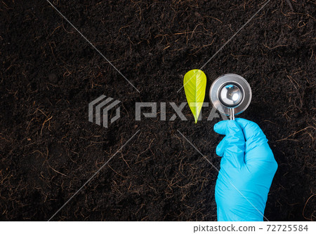 Hand of researcher holding a stethoscope on fertile black soil 72725584