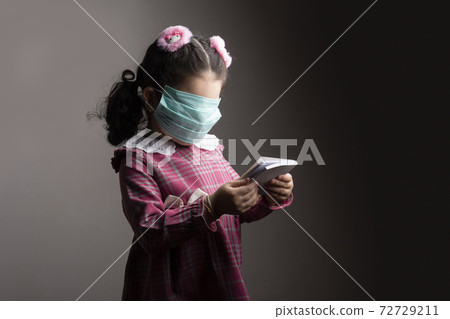 Covered face of a little girl with protection hospital mask when studying a book 72729211