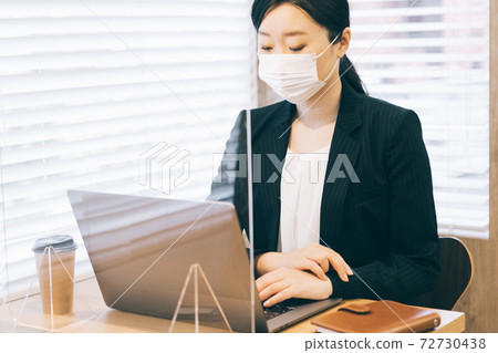 A woman in a mask working in front of a splash-proof acrylic board 72730438