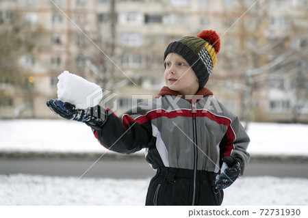 Child holds piece of snow in his hands. Boy playing snowballs 72731930
