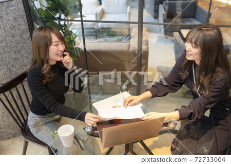 Two women having fun chatting while looking at a computer and materials 72733004