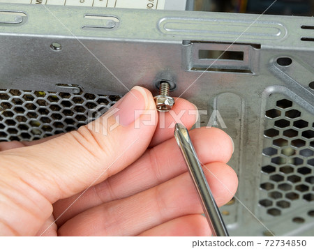 Woman fingers remove the screws holding the power supply unit in the tower case with a screwdriver.  72734850