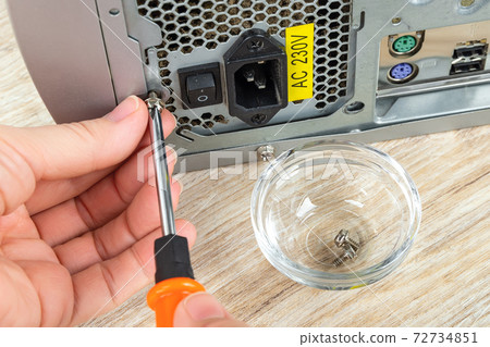 Woman hands remove the screw holding old power supply unit in a tower case with a screwdriver . 72734851