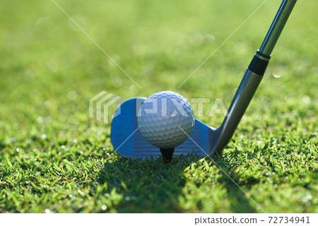 Golf clubs and golf balls on a green lawn in a beautiful golf course with morning sunshine.Close up of golf ball on a tee with the golf clubs ready to hit the ball. Golf clubs and golf balls on a green lawn in a beautiful golf course with morning sunshine.Close up of golf ball on a tee with the golf clubs ready to hit the ball. 72734941