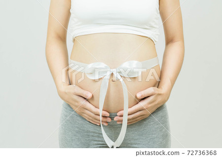 Selective focus of a tummy of a pregnant woman with festive white ribbon bow on tummy, isolated on gray background, body part, happy pregnancy time, new life concept 72736368