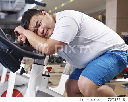 an overweight asian young man exhausted with exercising in fitness center 72737248