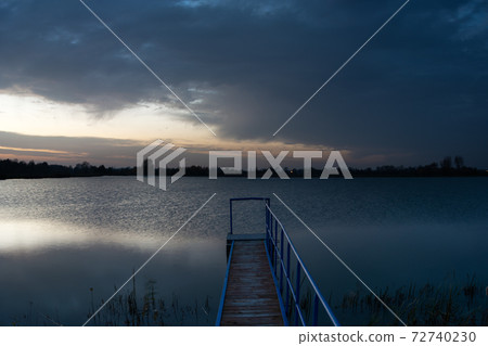 Bridge towards the lake and dark evening clouds 72740230