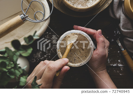 Starter sourdough. Female hands holding a jar with sourdough over wooden background. 72740945