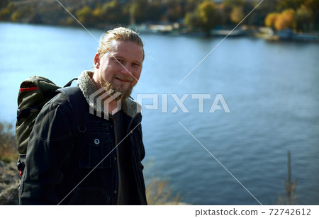A handsome lamber adventurer smiling at camera and standing on the edge of cliff . A beautiful autumn landscape and lake on background. Concept of people traveling in nature. A handsome lamber adventurer smiling at camera and standing on the edge of cliff . A beautiful autumn landscape and lake on background. Concept of people traveling in nature. 72742612