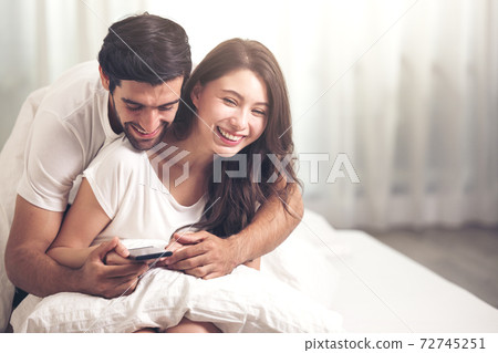 Attractive happy young couple laying on bed in the bedroom Attractive happy young couple laying on bed in the bedroom 72745251