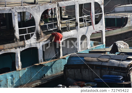 A mechanic man repairing an old hull of a medium-sized ship parked at Shodrugat, Dhaka, Bangladesh. 72745422
