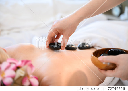 Young woman getting black hot stone on back her in spa salon 72746226