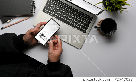 Male hands using smartphone while working with laptop on office desk 72747058