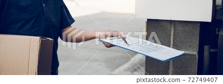 Young asian man smiling while delivering a cardboard box to the woman holding document to signing signature. 72749407