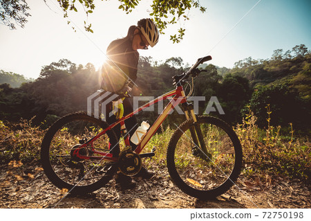 Woman cyclist adjust the seat height cycling on sunrise winter forest trail 72750198