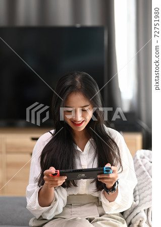 Portrait of young woman playing video game while sitting on sofa at home. 72751980