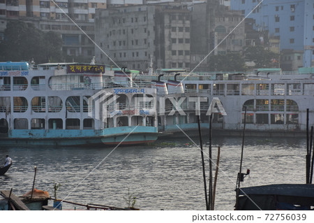 A medium-sized passenger ship parked at Shodrugat, Dhaka, Bangladesh, a building along the river or a building under construction 72756039