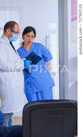 Doctor talking with assistant holding teeth x-ray Doctor talking with assistant holding teeth x-ray 72760519