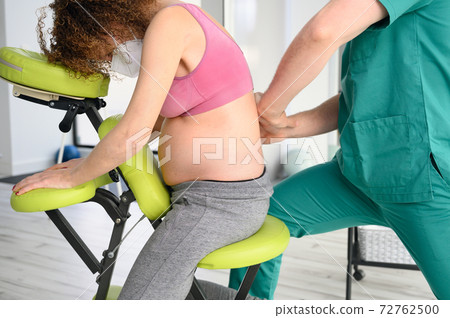 Male physiotherapist cures back pain of a pregnant woman. Male physiotherapist cures back pain of a pregnant woman. 72762500