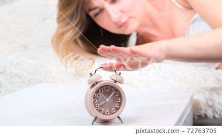 Woman in bed turns off the alarm clock in the morning. the woman does not want to get up early Woman in bed turns off the alarm clock in the morning. the woman does not want to get up early 72763705