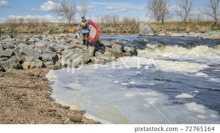 Paddler portaging paddleboard over river rapid Paddler portaging paddleboard over river rapid 72765164