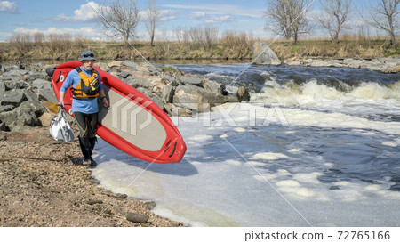 Paddler portaging paddleboard over river rapid Paddler portaging paddleboard over river rapid 72765166
