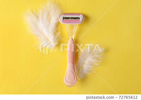 Razor and feathers on yellow background, place for text 72765612