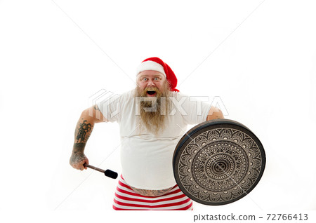 Isolated portrait on a white background of an overweigh happy and joyful man shaman with tattooed arms in Santa Claus hat dancing with a tambourine Isolated portrait on a white background of an overweigh happy and joyful man shaman with tattooed arms in Santa Claus hat dancing with a tambourine 72766413