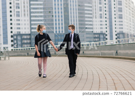 Schoolchildren, a boy and girl in medical masks walk in the city. Schoolchildren, a boy and girl in medical masks walk in the city. 72766621
