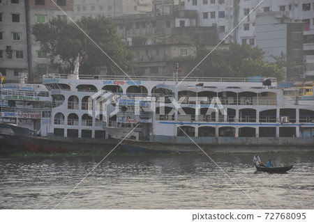 A medium-sized passenger ship parked at Shodrugat, Dhaka, Bangladesh, a small ferry crossing the river 72768095