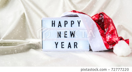 Lightbox with text HAPPY NEW YEAR with santa hat on silk fabric background. Winter holiday concept. 72777220