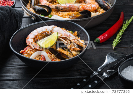 Homemade spanish seafood paella in frying pan and black bowl on black wooden background Homemade spanish seafood paella in frying pan and black bowl on black wooden background 72777295