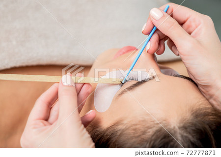 Woman receiving eyelash extension procedure. 72777871