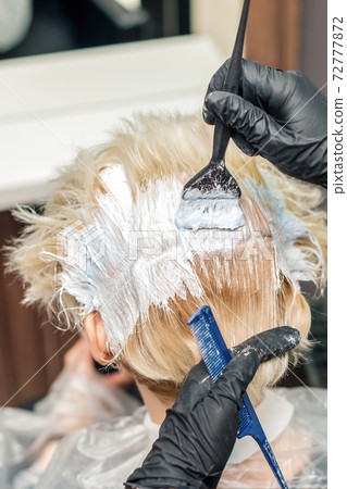 Hairdresser hands in black gloves are painting the female hair in a white color close up. 72777872