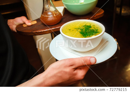 The waiter holds a plate of chicken broth The waiter holds a plate of chicken broth 72779215