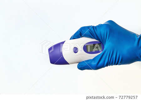 A hand in a protective glove holds an electronic non-contact thermometer. Temperature Measurement Device on white background 72779257