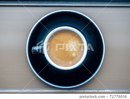 Top view for coffee in black ceramic cup with round dish beneath on table Top view for coffee in black ceramic cup with round dish beneath on table 72779836