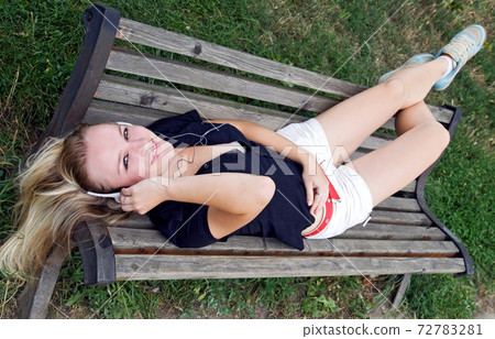 Teenage girl lying on a bench and listen music. 72783281