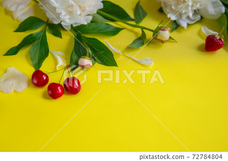 Flowers of peony, branches, leaves and petals and berries of cherry, strawberry with space for text on a yellow background. Flat lay, top view. 72784804