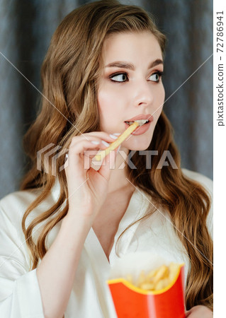 beautiful young woman with long hair and makeup eating French fries. 72786941