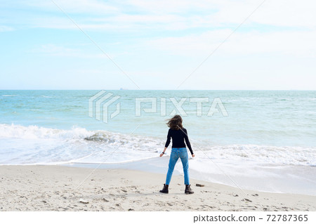 Young woman with dark hair alone relaxing at the sea shore. 72787365