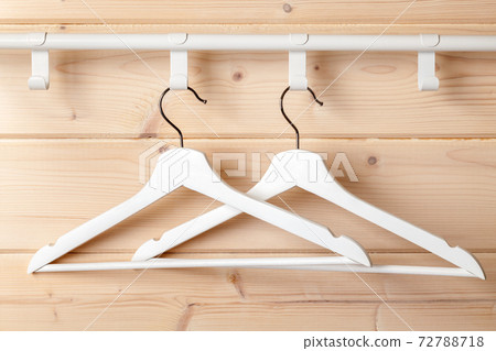 Two white hangers hang near natural wooden wall Two white hangers hang near natural wooden wall 72788718