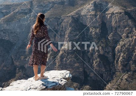 Long haired brunette stands on dangerous rocky cliff edge Long haired brunette stands on dangerous rocky cliff edge 72790067