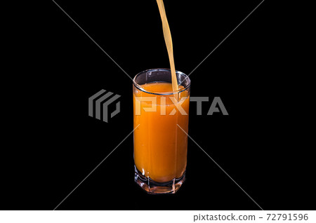Freshly squeezed fruit juice is poured into a glass. Peach, orange or carrot on an isolated black background. Freshly squeezed fruit juice is poured into a glass. Peach, orange or carrot on an isolated black background. 72791596