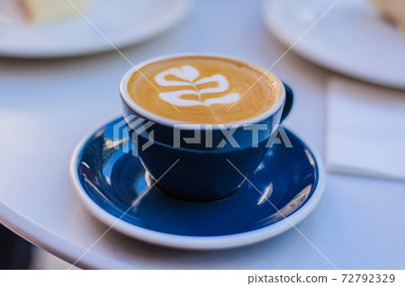 aromatic coffee cappuccino in a blue cup on a saucer stands on a white table 72792329