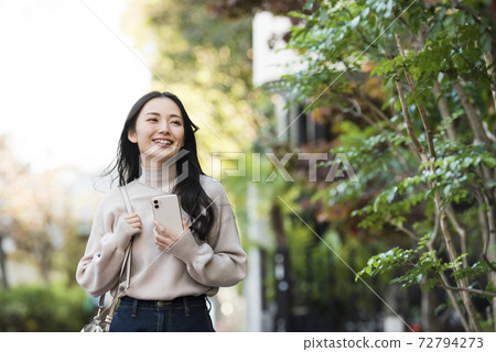 A young woman walking with a smartphone 72794273