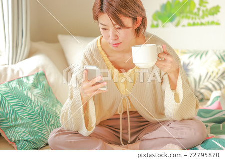 一個女人坐在一起的咖啡杯,看著她的智能手機 一個女人坐在一起的咖啡杯,看著她的智能手機 72795870