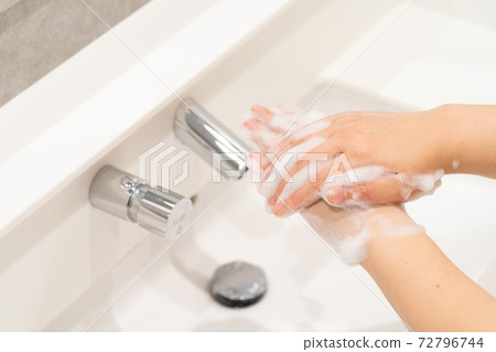 A woman washing her hands in a washbasin with an automatic faucet 72796744