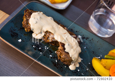 Tasty veal steak with pepper sauce and baked potatoes at plate Tasty veal steak with pepper sauce and baked potatoes at plate 72802410