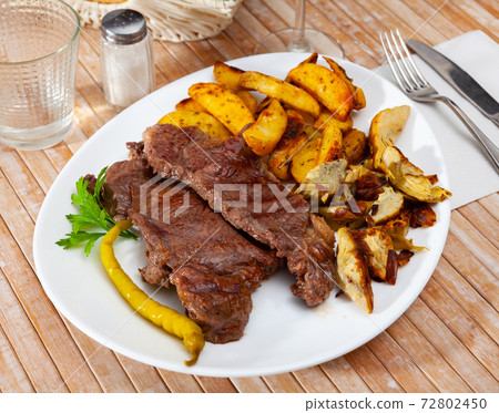 Delicious beef steak with baked potatoes and artichokes Delicious beef steak with baked potatoes and artichokes 72802450
